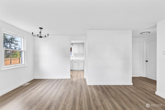 unfurnished room with light wood-type flooring and an inviting chandelier