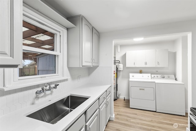 laundry room with water heater, washer and clothes dryer, light wood-type flooring, cabinets, and sink