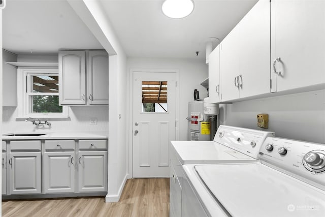 laundry room featuring washing machine and dryer, cabinets, secured water heater, a healthy amount of sunlight, and sink