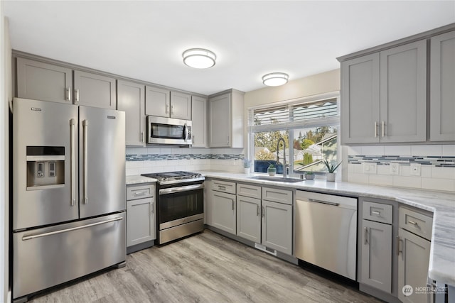 kitchen featuring light stone countertops, appliances with stainless steel finishes, light hardwood / wood-style floors, and tasteful backsplash