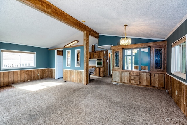 unfurnished living room with a textured ceiling, a chandelier, wooden walls, and carpet flooring