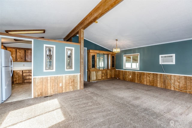 unfurnished living room featuring a wall unit AC, light carpet, lofted ceiling with beams, an inviting chandelier, and wood walls