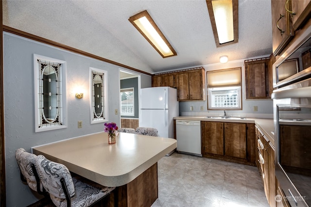 kitchen with a breakfast bar area, sink, vaulted ceiling, a textured ceiling, and white appliances