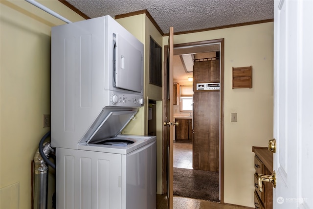 laundry room featuring a textured ceiling, ornamental molding, and stacked washer and clothes dryer