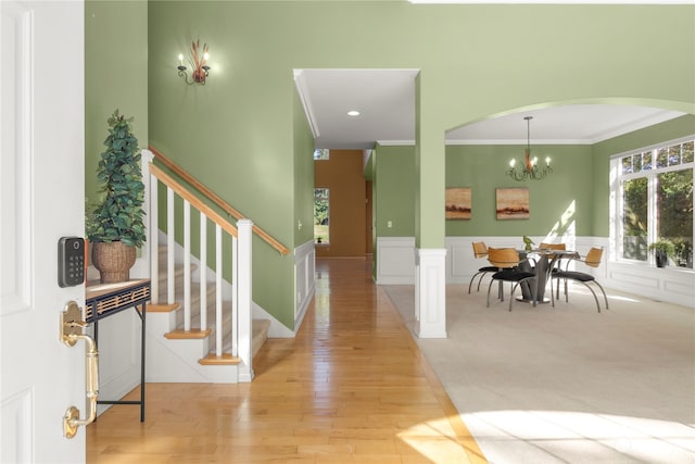 entrance foyer with ornamental molding, light wood-type flooring, and an inviting chandelier