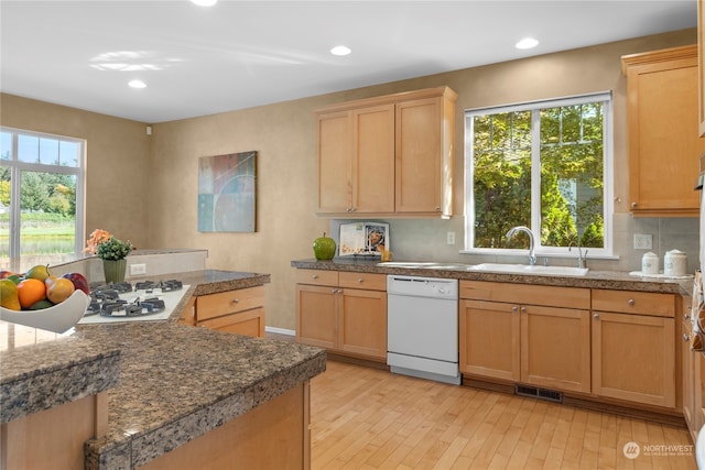 kitchen with white appliances, light wood-type flooring, a healthy amount of sunlight, sink, and tasteful backsplash