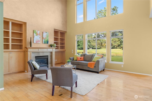 living room with a towering ceiling, a tile fireplace, built in features, and light hardwood / wood-style flooring