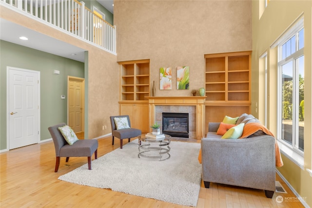 living room with a tiled fireplace, built in features, a towering ceiling, and hardwood / wood-style flooring