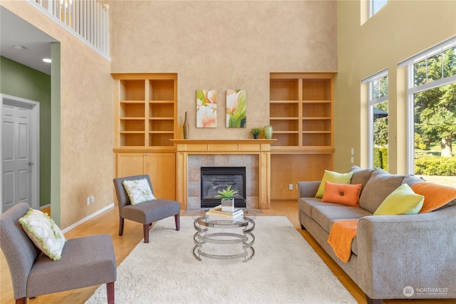 living room featuring a towering ceiling, a fireplace, built in features, and a healthy amount of sunlight