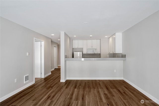 kitchen featuring white appliances, kitchen peninsula, white cabinetry, and dark wood-type flooring