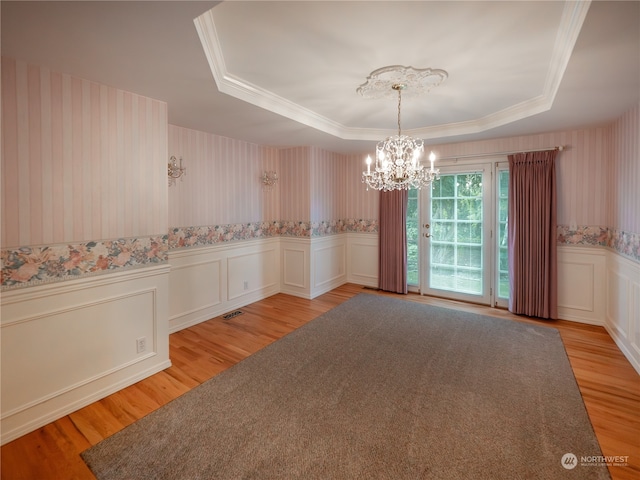 unfurnished room with a tray ceiling, light hardwood / wood-style flooring, and an inviting chandelier