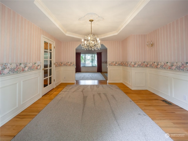 dining space featuring an inviting chandelier, ornamental molding, a tray ceiling, and light hardwood / wood-style floors