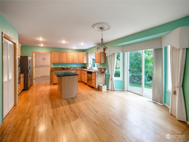 kitchen with sink, light wood-type flooring, a kitchen island, stainless steel appliances, and decorative light fixtures