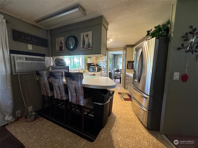 kitchen with sink, kitchen peninsula, stainless steel fridge, a wall mounted AC, and a breakfast bar