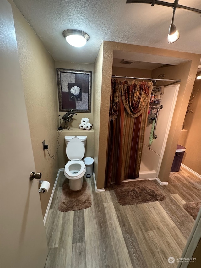 bathroom featuring toilet, hardwood / wood-style flooring, walk in shower, and a textured ceiling