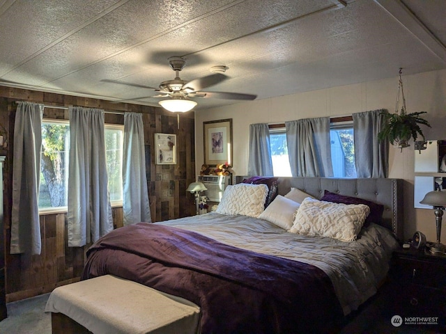 bedroom featuring wooden walls, a textured ceiling, and ceiling fan