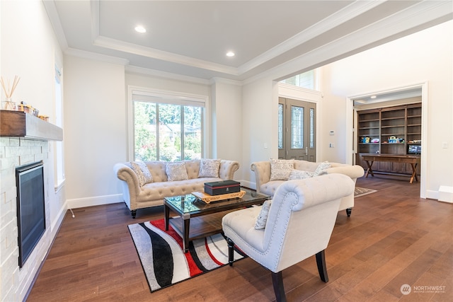 living room featuring a tray ceiling, crown molding, a fireplace, and dark hardwood / wood-style flooring