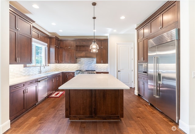 kitchen with built in appliances, hanging light fixtures, dark hardwood / wood-style floors, and a kitchen island