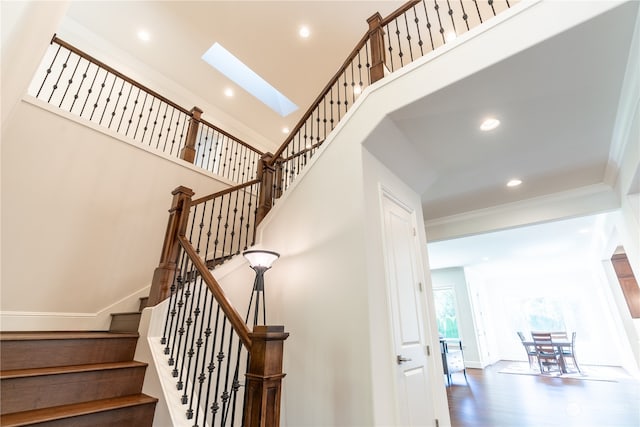 stairs featuring ornamental molding, a towering ceiling, a skylight, and hardwood / wood-style floors