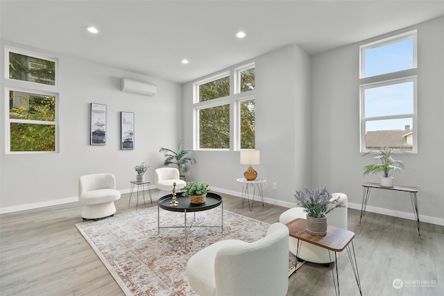 sitting room featuring a wall unit AC, wood-type flooring, and a healthy amount of sunlight