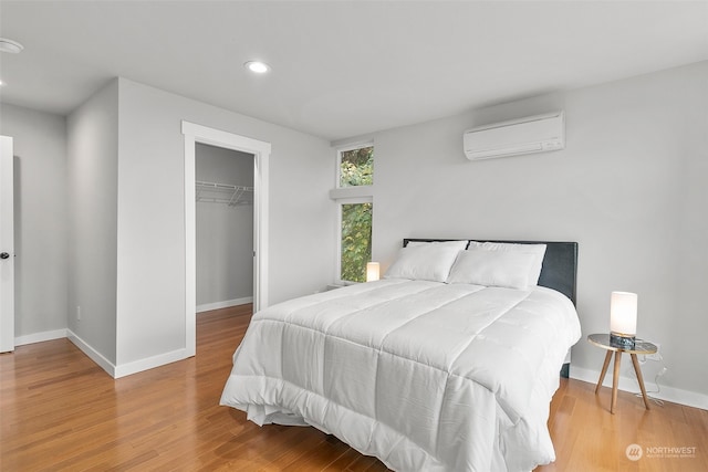 bedroom with a closet, a wall unit AC, a spacious closet, and hardwood / wood-style flooring