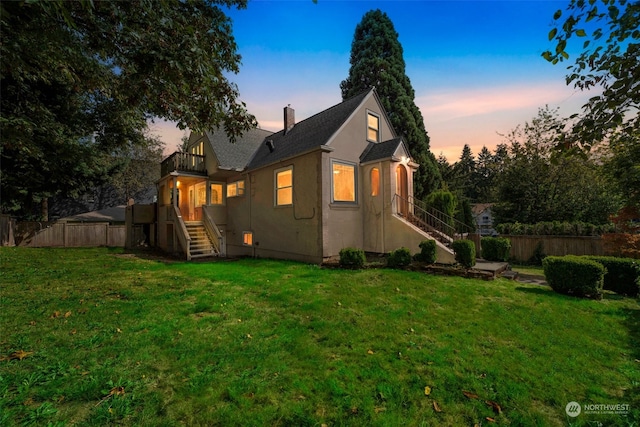 back house at dusk featuring a lawn and a balcony