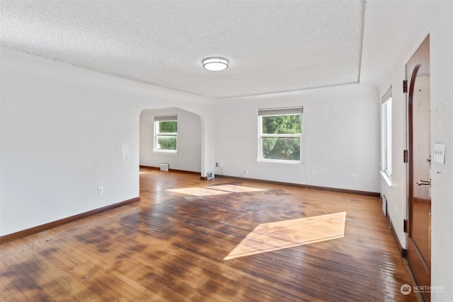 unfurnished room with a textured ceiling, wood-type flooring, and a wealth of natural light