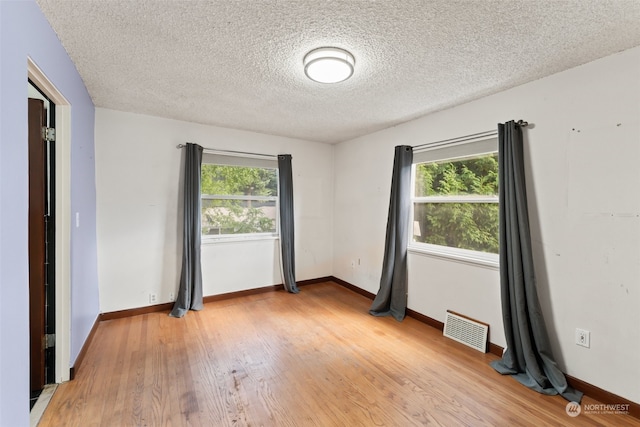 spare room featuring a textured ceiling, light hardwood / wood-style flooring, and a wealth of natural light