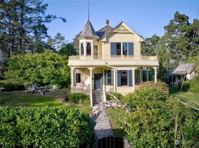 victorian house featuring a balcony, covered porch, and a front yard