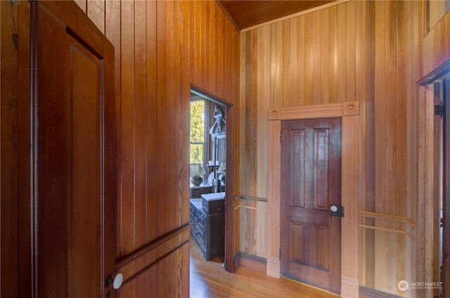 corridor with light hardwood / wood-style floors and wooden walls