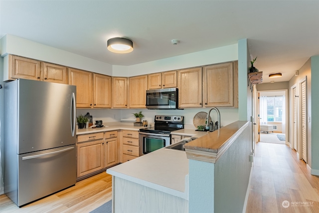 kitchen with light brown cabinetry, kitchen peninsula, light hardwood / wood-style flooring, and stainless steel appliances