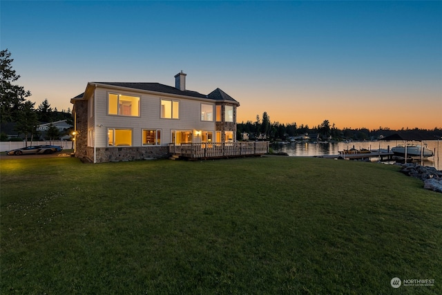 back house at dusk with a lawn and a deck with water view