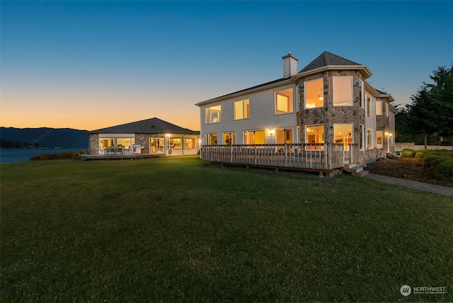 back house at dusk with a deck with mountain view and a lawn