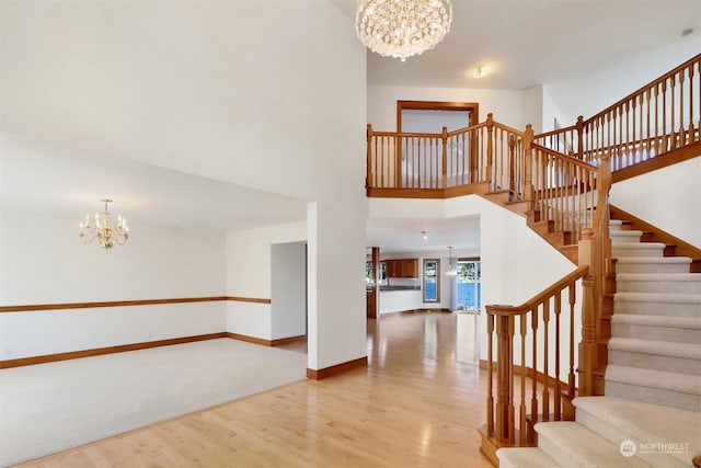 stairway with a towering ceiling, a chandelier, and wood-type flooring