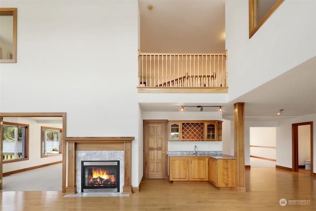 unfurnished living room with a high ceiling, light wood-type flooring, a premium fireplace, and wet bar