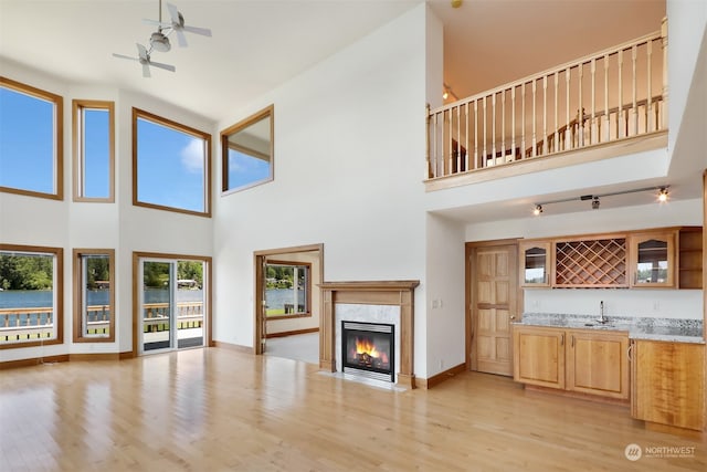 unfurnished living room with a high ceiling, light wood-type flooring, a fireplace, and ceiling fan