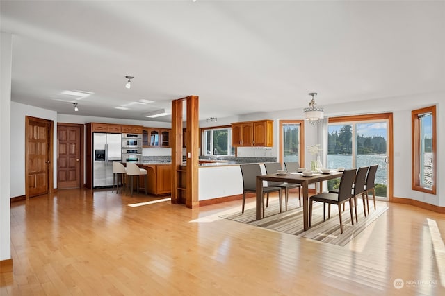 dining space featuring light wood-type flooring, a notable chandelier, and a water view