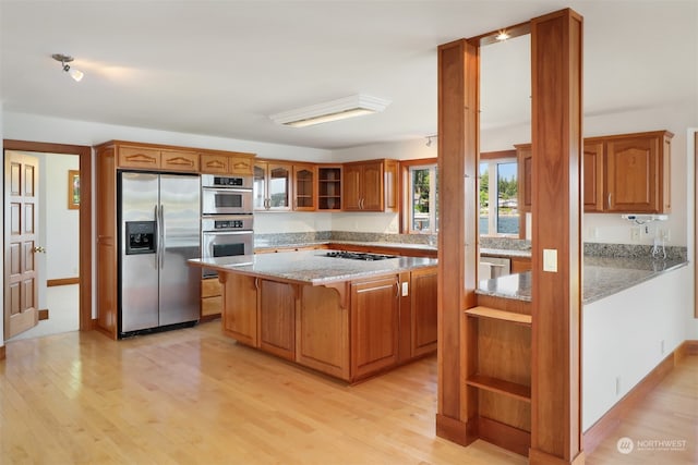 kitchen with light stone counters, stainless steel appliances, a center island, and light hardwood / wood-style flooring