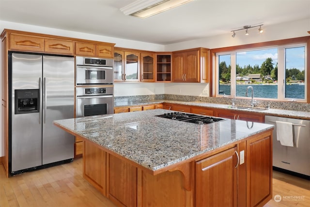 kitchen featuring light hardwood / wood-style floors, a kitchen island, sink, light stone countertops, and appliances with stainless steel finishes