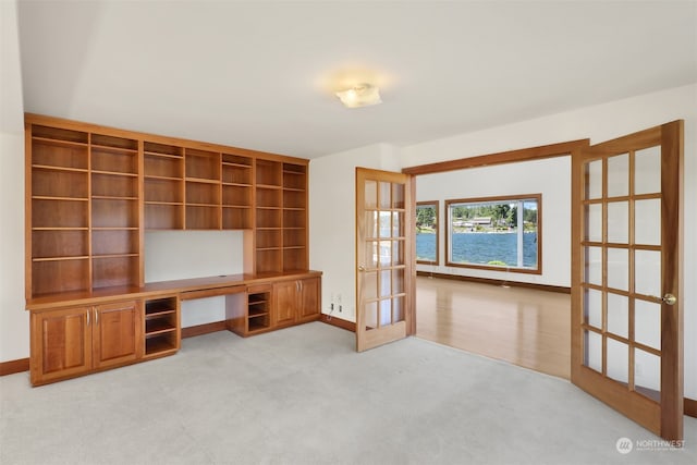 unfurnished living room with a water view, french doors, and light colored carpet