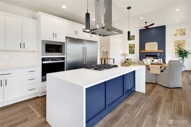 kitchen with appliances with stainless steel finishes, light hardwood / wood-style floors, white cabinetry, island range hood, and decorative light fixtures