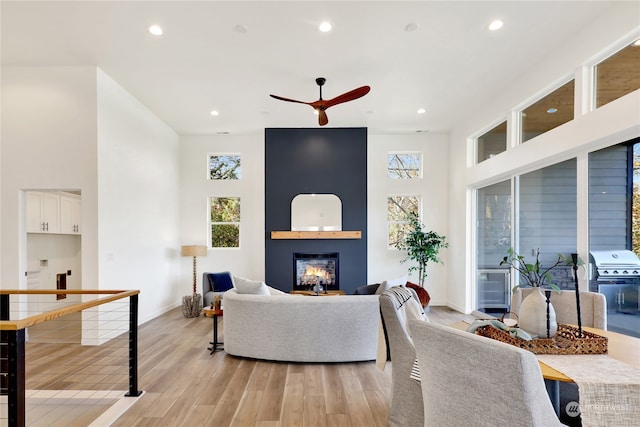 living room featuring light wood-type flooring, ceiling fan, and a high ceiling