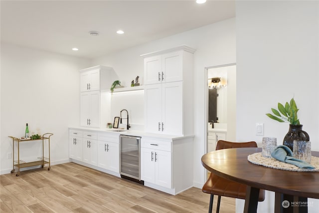 bar featuring sink, light hardwood / wood-style flooring, wine cooler, and white cabinets