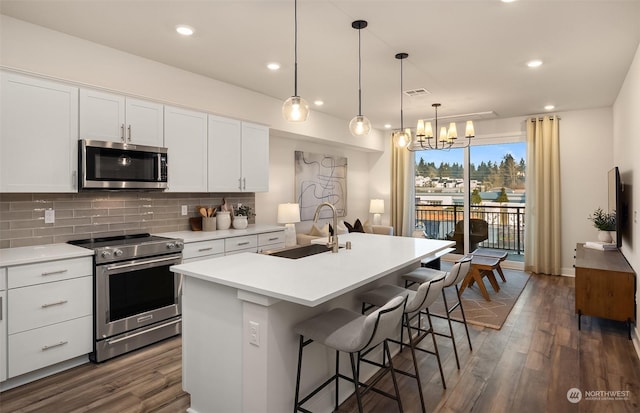 kitchen with stainless steel appliances, white cabinetry, sink, and a center island with sink