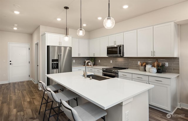 kitchen with decorative light fixtures, stainless steel appliances, an island with sink, and white cabinets