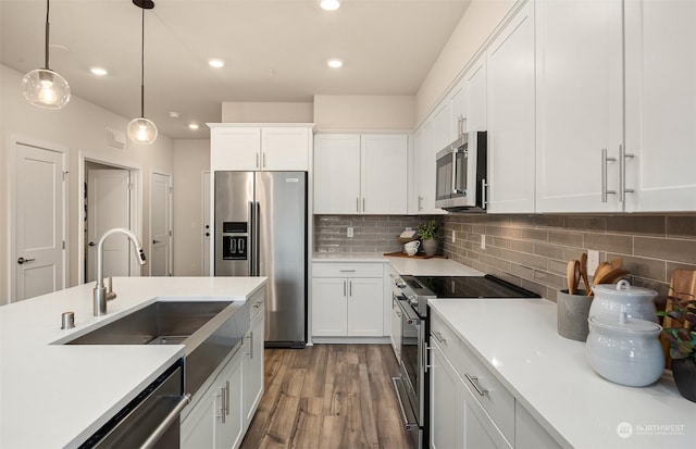 kitchen with sink, hardwood / wood-style flooring, appliances with stainless steel finishes, hanging light fixtures, and white cabinets