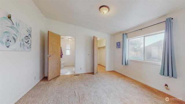 unfurnished bedroom featuring carpet, a spacious closet, lofted ceiling, connected bathroom, and baseboards