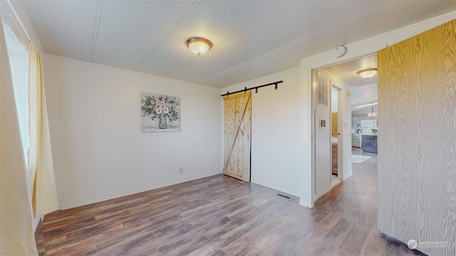 unfurnished bedroom with a barn door, baseboards, wood finished floors, and visible vents