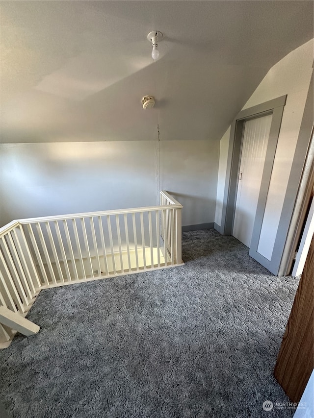 hallway with lofted ceiling and dark colored carpet