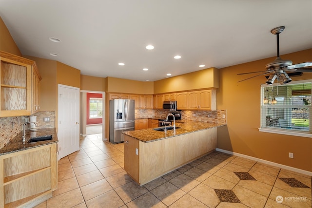 kitchen with kitchen peninsula, stainless steel appliances, stone counters, light brown cabinetry, and sink